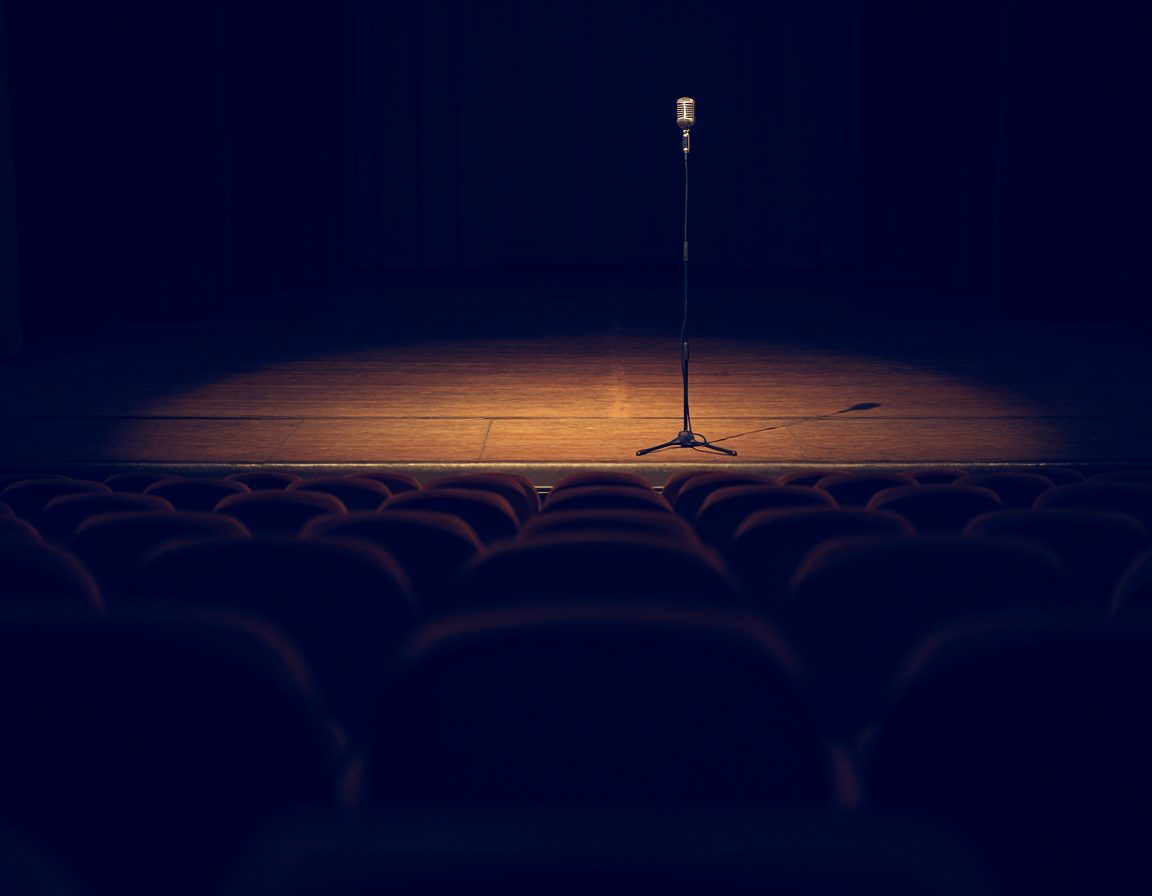 Microphone on an empty stage under a single spotlight, facing rows of empty seats